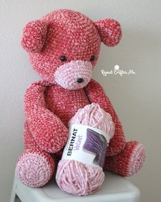 a crocheted teddy bear sitting on top of a stool holding a ball of yarn