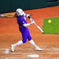 a woman swinging a baseball bat at a ball on a field with grass in the background