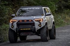 the front end of a silver toyota truck driving down a dirt road