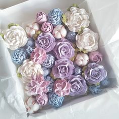 a box filled with cupcakes covered in pink and blue frosting flowers on top of white paper