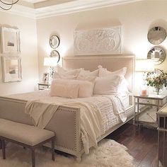 a bedroom with white bedding and lots of mirrors on the wall, along with a bench