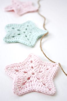 three crocheted stars are hanging from a string on a white surface, one is pink and the other is blue