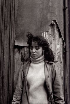 a black and white photo of a woman standing in front of an old wooden door