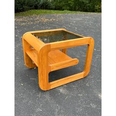 a wooden table sitting on top of a parking lot next to grass and trees in the background