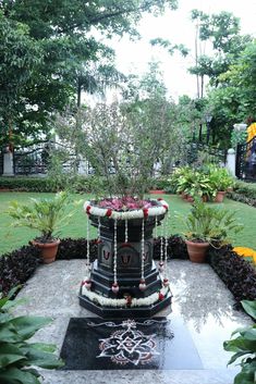 a fountain in the middle of a garden surrounded by flowers and plants with chains hanging from it's sides