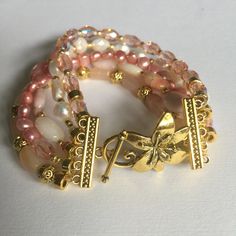 Beautiful, unique beaded freshwater pearl bracelet made with pink and natural cream pearls, gorgeous pink opal and moonstone beads, brilliant Swarovski crystals and gold plated beads. This beautiful, one of a kind statement bracelet closes with an ornate floral toggle clasp. This luxurious bracelet measures 7.5 inches (19.05cm) total. If you love to receive compliments on your jewelry, just wait until you wear this gorgeous bracelet. Stunningly beautiful, the perfect gift for any occasion. Pleas Multi-strand Pearl Bracelets As Gift, Gold Beaded Bracelets With Pearl And Gemstone Beads, Gold Pearl Bracelets With Gemstone Beads, Multi-strand Pearl Bracelet As Gift, Pink Pearl Jewelry With Natural Stones, Elegant Multi-strand Gemstone Beaded Bracelets, Pink Pearl Jewelry With Gemstone Beads, Pink Pearl Jewelry With Faceted Beads, Bohemian Gold Pearl Bracelet With Gemstone Beads