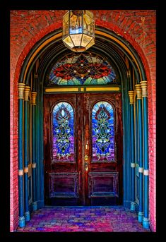 an ornate doorway with two stained glass doors and blue brick walls, leading to the front door