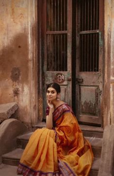 a woman in an orange sari sitting on steps next to a door and looking at the camera