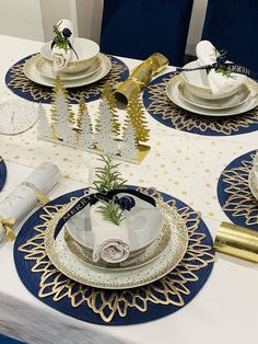 the table is set with blue and white plates, napkins, gold trimmings