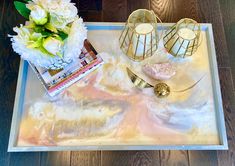 a tray with candles, flowers and magazines on it sitting on a wooden floor next to a vase