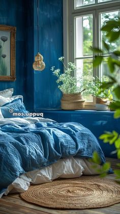 a bedroom with blue walls and white bedding in front of a large window, potted plant on the far wall