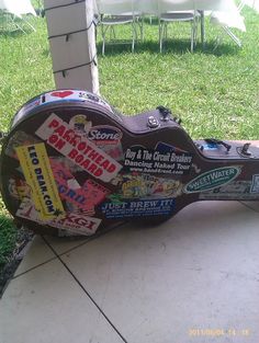 a guitar sitting on top of a sidewalk next to a grass covered yard with white tables and chairs in the background