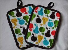 two oven mitts with apples, pears and leaves printed on them sitting on a white surface