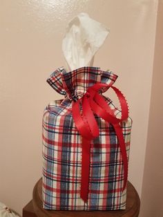 a plaid wrapped gift box with red ribbon and tissue paper on top, sitting on a wooden stand