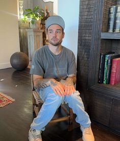 a man sitting in a chair with his legs crossed, wearing a hat and looking at the camera