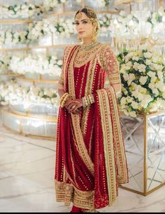 a woman in a red and gold outfit standing next to a flower display with white flowers