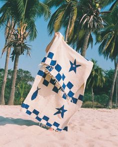 a beach towel with blue and white stars on it sitting in the sand under palm trees