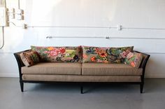 a couch sitting in front of a white wall with floral pillows on it's back