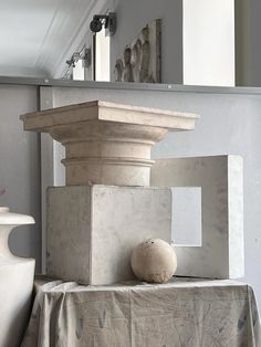 a white vase sitting on top of a table next to a stone block and pillar