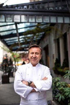 a man wearing a chef's coat standing in front of a building with his arms crossed