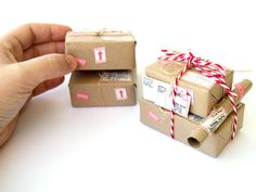 a hand holding a piece of brown paper with red and white tags on it next to two small boxes