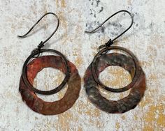 two pairs of metal earrings on top of a wooden table with rusted paint and black wire