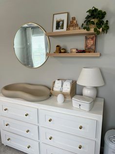 a white dresser topped with lots of drawers and a round mirror above it's top