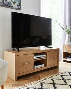 a flat screen tv sitting on top of a wooden entertainment center next to a window