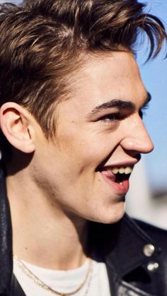 a close up of a person wearing a leather jacket and smiling at the camera with his hair pulled back