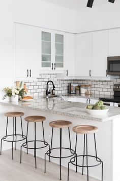 three stools sit at the bar in this white kitchen