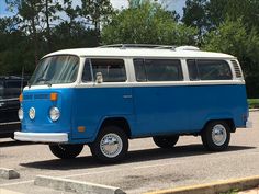 an old blue and white van parked in a parking lot next to another black car