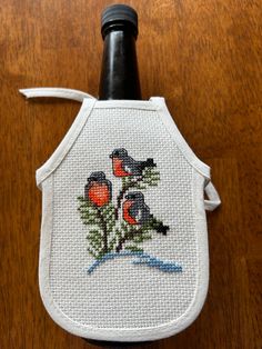 a cross - stitched bottle cover with three birds on it sitting on top of a wooden table