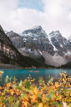 the mountains are covered with snow and green plants in front of a blue body of water