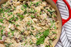 a red skillet filled with pasta and peas on top of a white table cloth