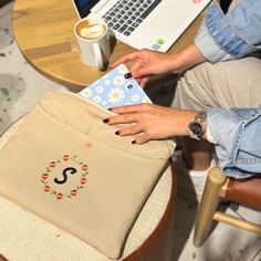 a woman sitting at a table with a laptop and bag on her lap, next to a cup of coffee