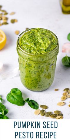 pumpkin seed pesto recipe in a glass jar with spinach leaves and seeds around it