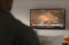 a man looking at a television screen with a large explosion in the background