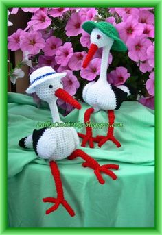 two crocheted birds wearing hats and sitting on a table with flowers in the background