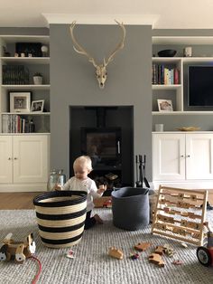 a baby sitting on the floor in front of a fire place with toys around it