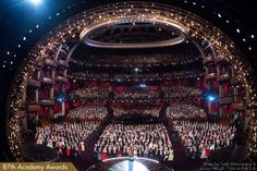 an auditorium full of people in red and white dresses with lights on the ceiling are looking towards the stage