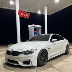 a white car is parked in front of a gas station at night with its lights on