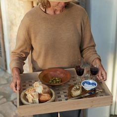 an older woman holding a tray with food and wine