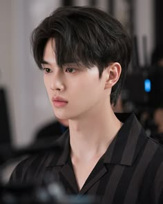 a young man with black hair is looking at the camera while wearing a black and white striped shirt