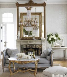 a living room filled with furniture and a chandelier above a fire place in front of a mirror