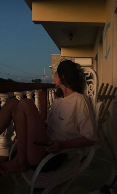 a woman sitting on top of a white chair next to a balcony under a blue sky