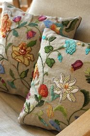 two pillows sitting on top of a white couch next to a wooden table with flowers