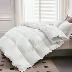 a white comforter sitting on top of a bed in a bedroom next to a window