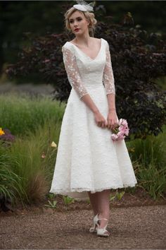 a woman wearing a white dress and holding a flower in her hand is posing for the camera