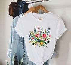 Please note that this shirt is a PRINTED version, meaning that the embroidery design is printed on a flat surface rather than being physically embroidered. While it may not have the tactile feel of actual embroidery, the printed design still adds a touch of elegance and style to the shirt. Trending right now printed embroidery tshirts for women, Garden Shirt, Wildflower Shirt, Floral Tee, Flower Tshirt, Vintage Wildflowers, Wild Flowers Shirt, Vintage Floral Shirt, Botanical Tshirt, Dainty Flowe White Floral Embroidered T-shirt For Spring, Multicolor Floral Embroidery T-shirt For Summer, Casual Multicolor Floral Embroidery T-shirt, Casual Multicolor T-shirt With Floral Embroidery, Spring Embroidered Relaxed Fit T-shirt, Multicolor Cotton Tops With Embroidered Graphics, Embroidered Relaxed Fit T-shirt For Spring, Multicolor Printed Tops For Spring, Spring Shirt With Multicolor Floral Embroidery