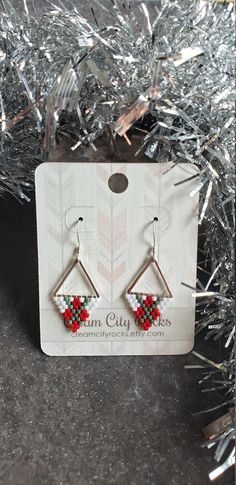 a pair of red, green and white beaded earrings sitting on top of a christmas tree